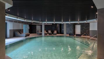 An indoor swimming pool with clear water, modern seating, and a dark ceiling.