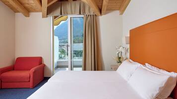 Ein Hotelzimmer mit einem Bett, einem roten Sessel, einem Fenster mit Bergblick und einer Holzbalkendecke.