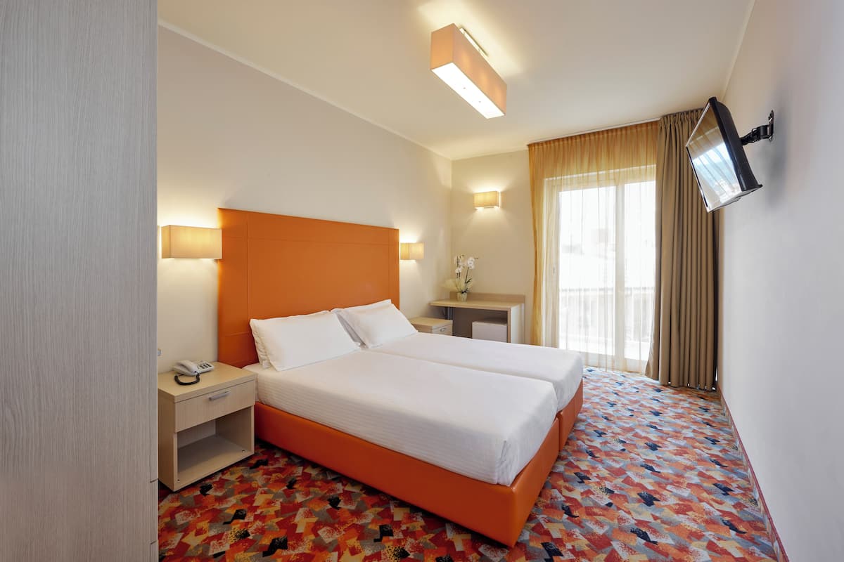 Une chambre d’hôtel avec un lit double, une table de chevet avec une lampe, un petit bureau et un téléviseur fixé au mur.