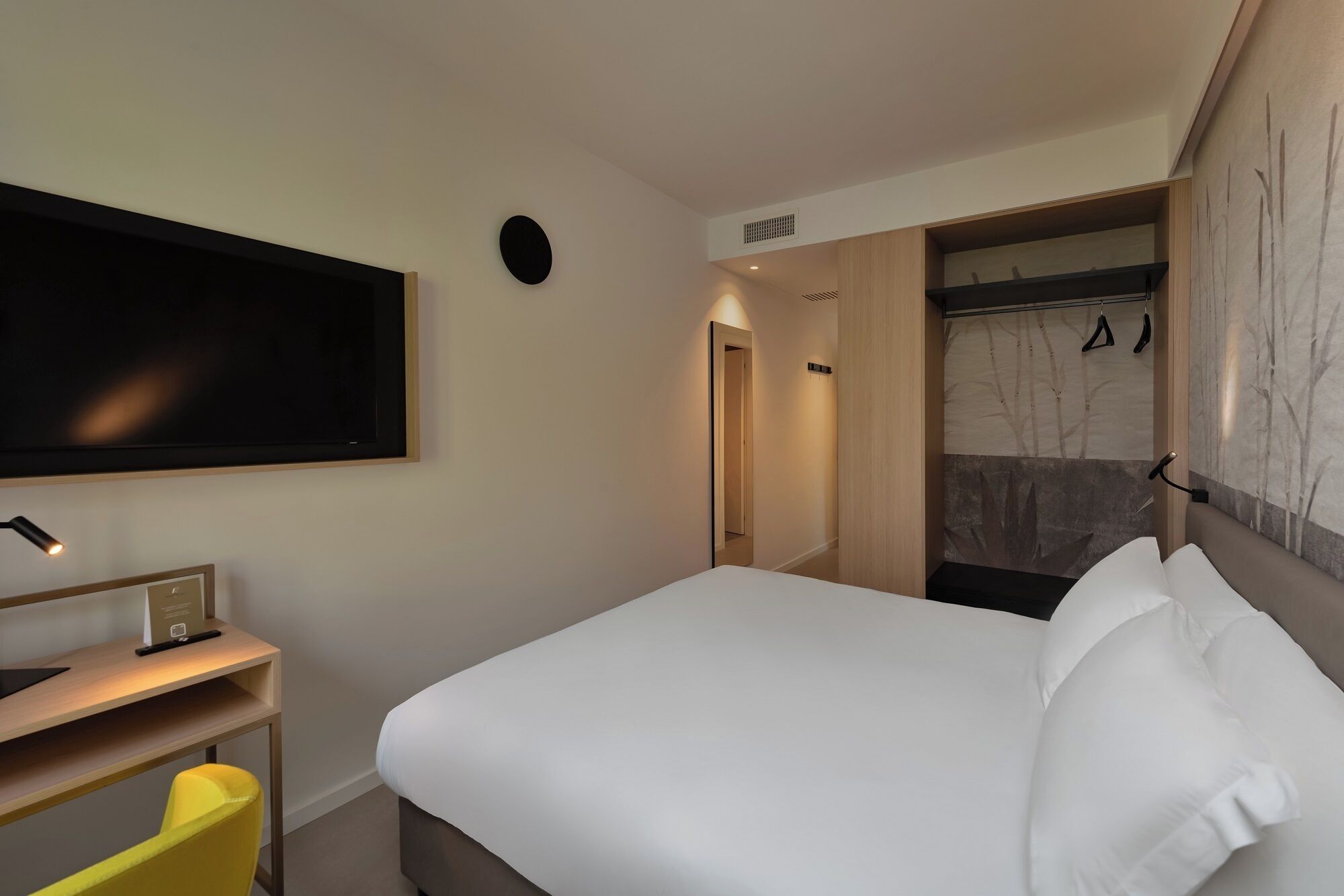 A hotel room with a bed, a desk, a chair, a TV, and a shower area.