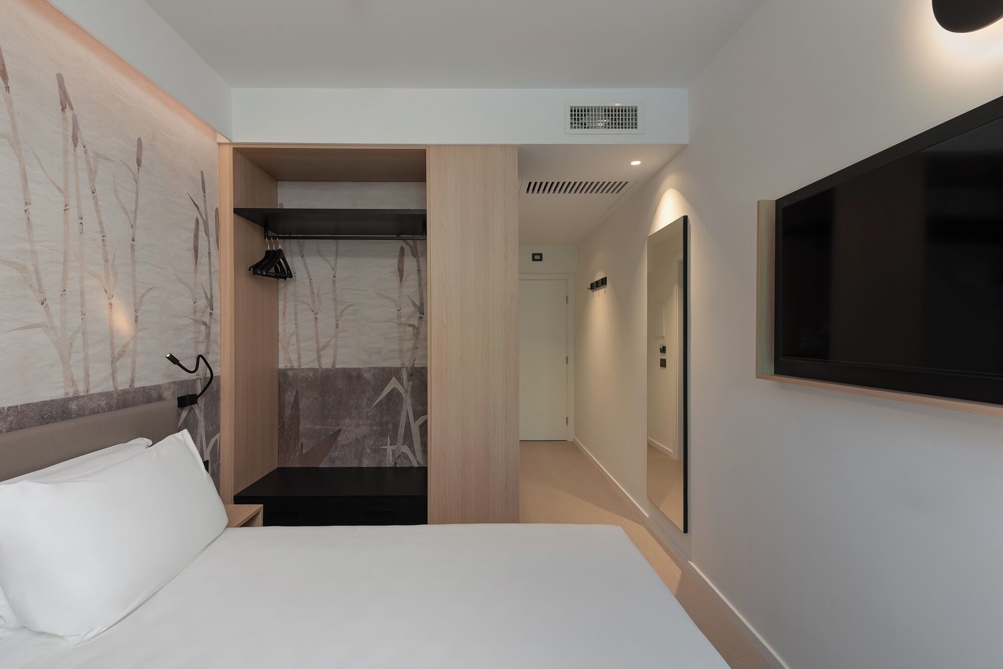 Et moderne hotelværelse med seng, fjernsyn, bruseområde og en gang til en dør.