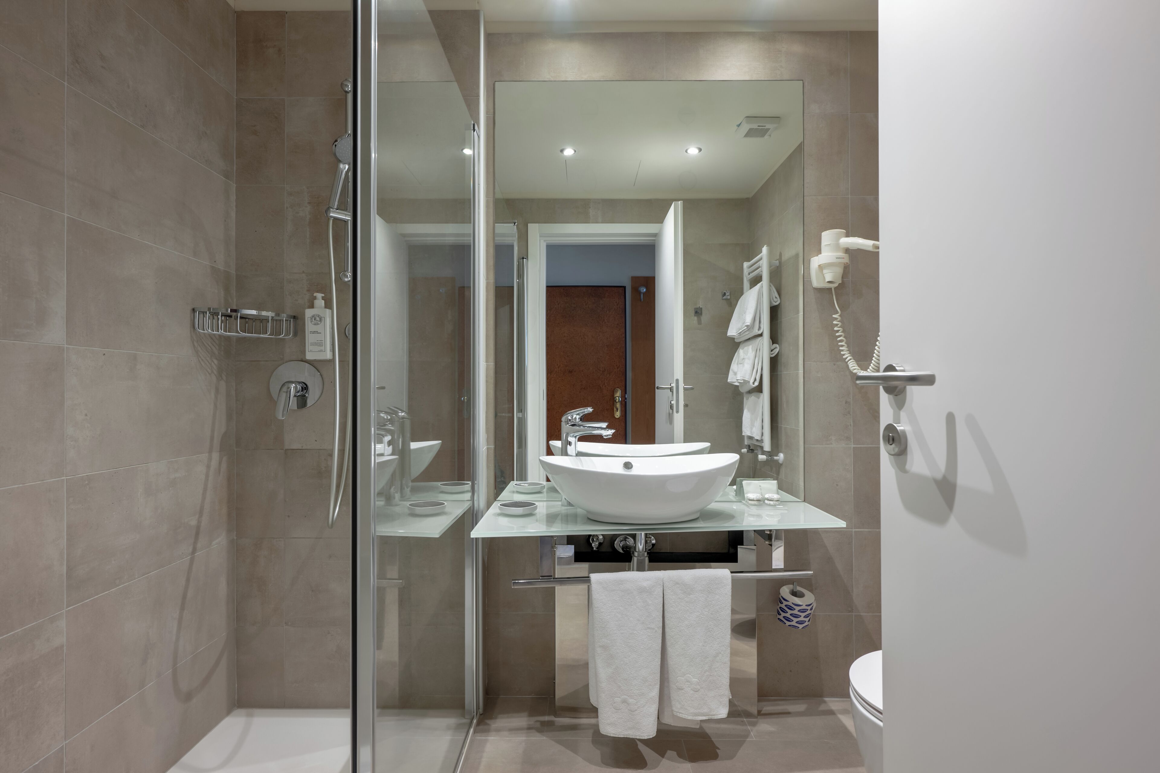 Een moderne badkamer met een douchecabine van glas, een witte wastafel en een zichtbaar toilet.