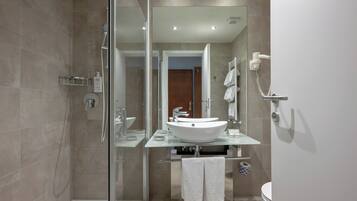 Een moderne badkamer met een douchecabine van glas, een witte wastafel en een zichtbaar toilet.