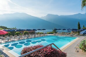 A pool with lounge chairs and umbrellas, surrounded by mountains and a view of the lake. - Hotel Royal Village (Limone sul Garda)