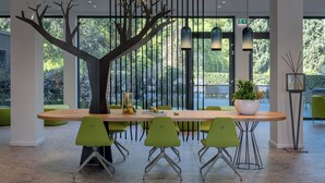 A modern dining area with a wooden table, green chairs, a decorative tree sculpture, and large windows with a view of greenery. - Hotel Royal Village (Limone sul Garda)