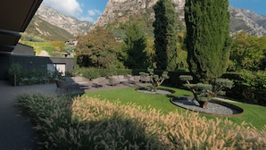 A landscaped garden with a seating area, a tall tree, and a mountain backdrop. - Hotel Royal Village (Limone sul Garda)