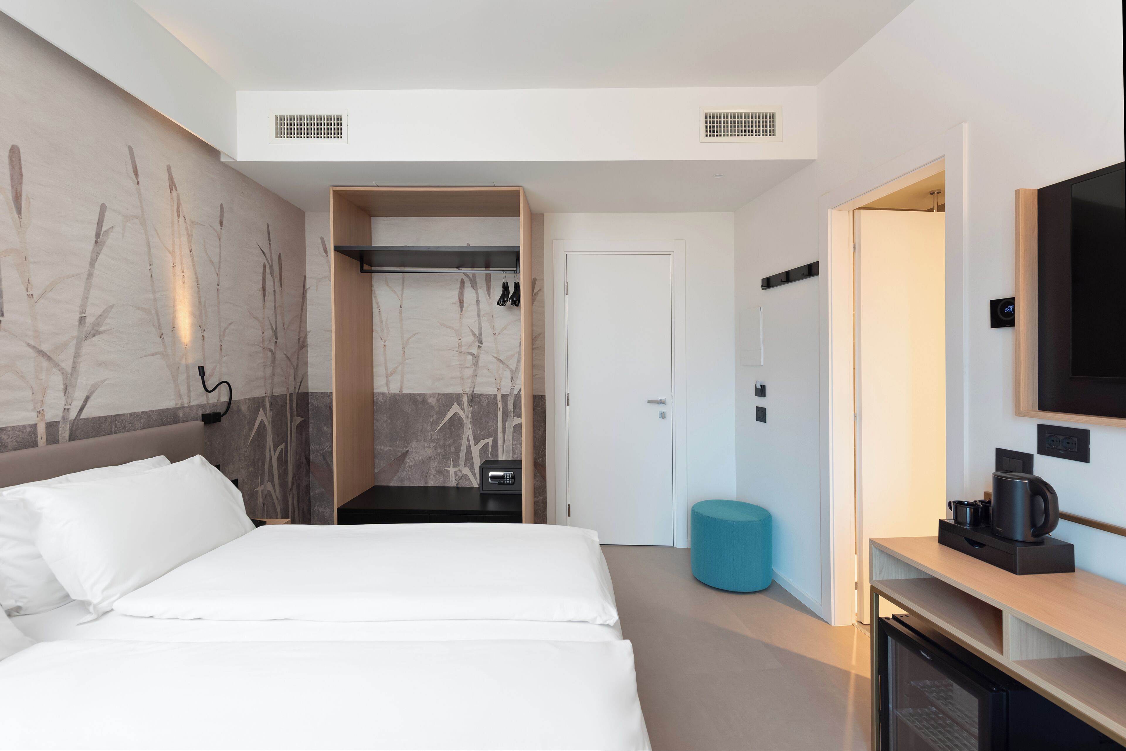 A modern hotel room with a large bed, a walk-in closet, a television, and a coffee maker.