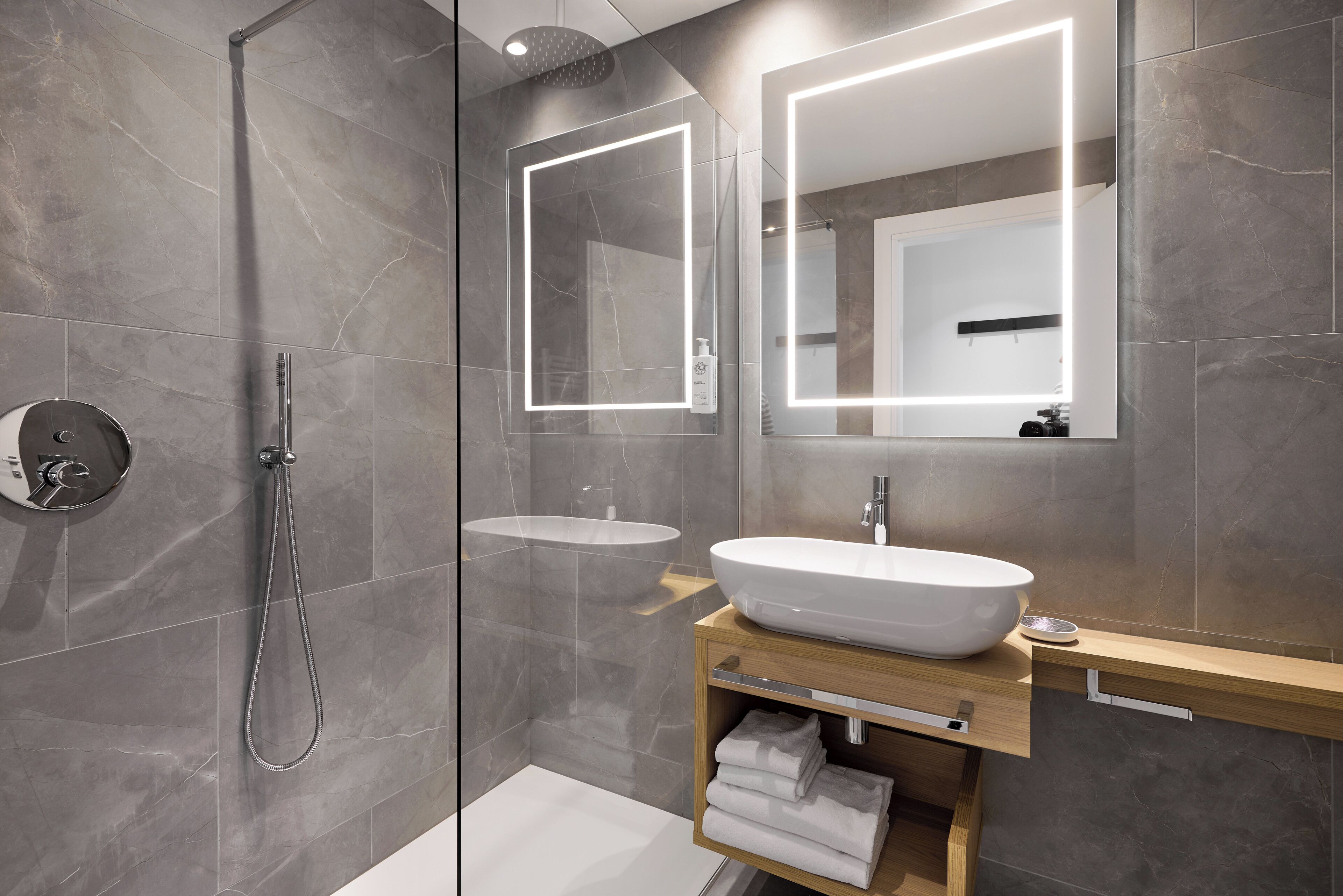 A modern bathroom with a glass-enclosed shower, a white vessel sink, and a wooden vanity with a mirror.