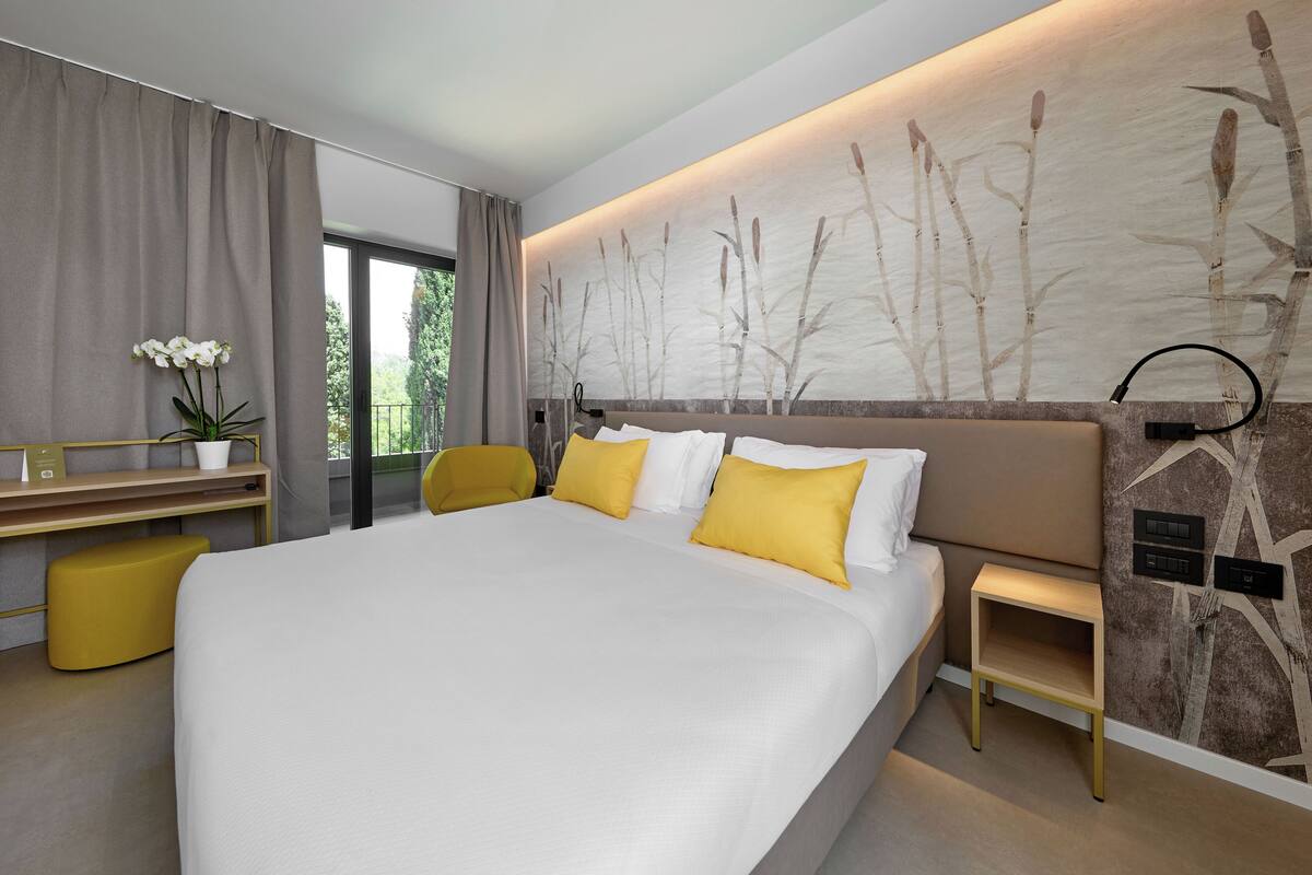 Une chambre d’hôtel moderne, dotée d’un grand lit, d’un bureau, d’une chaise et offrant une vue sur la verdure environnante.