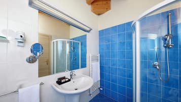 Un baño con un lavamanos blanco, azulejos azules, una cabina de ducha de vidrio y una viga de techo de madera.