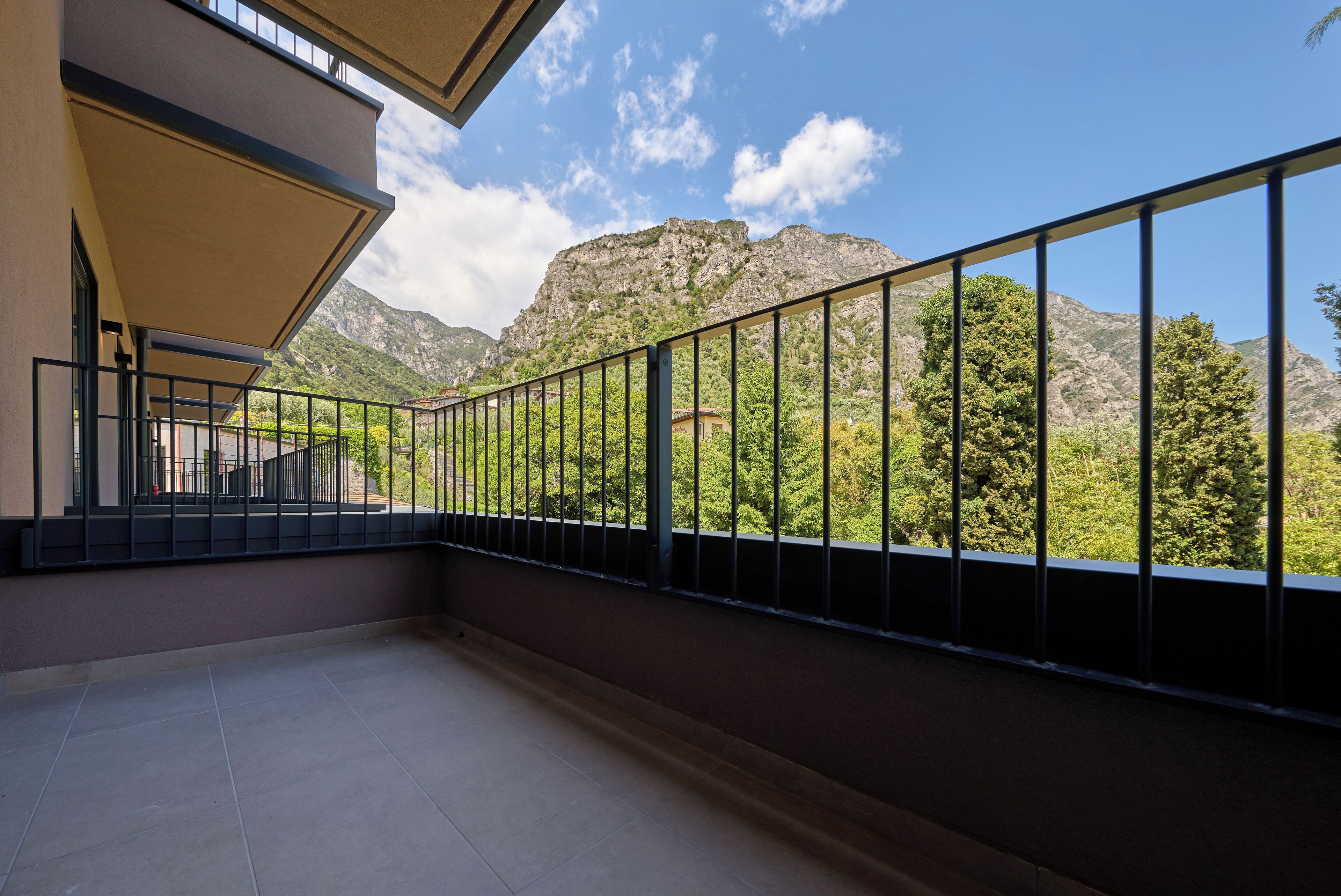 Un balcon doté d’une rambarde en métal, d’un sol carrelé et offrant une vue sur les montagnes et la verdure.