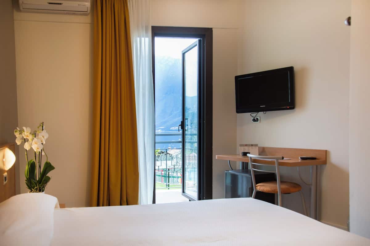 Une chambre d’hôtel comprenant un lit, un bureau avec une chaise, une télévision et une fenêtre avec des rideaux.