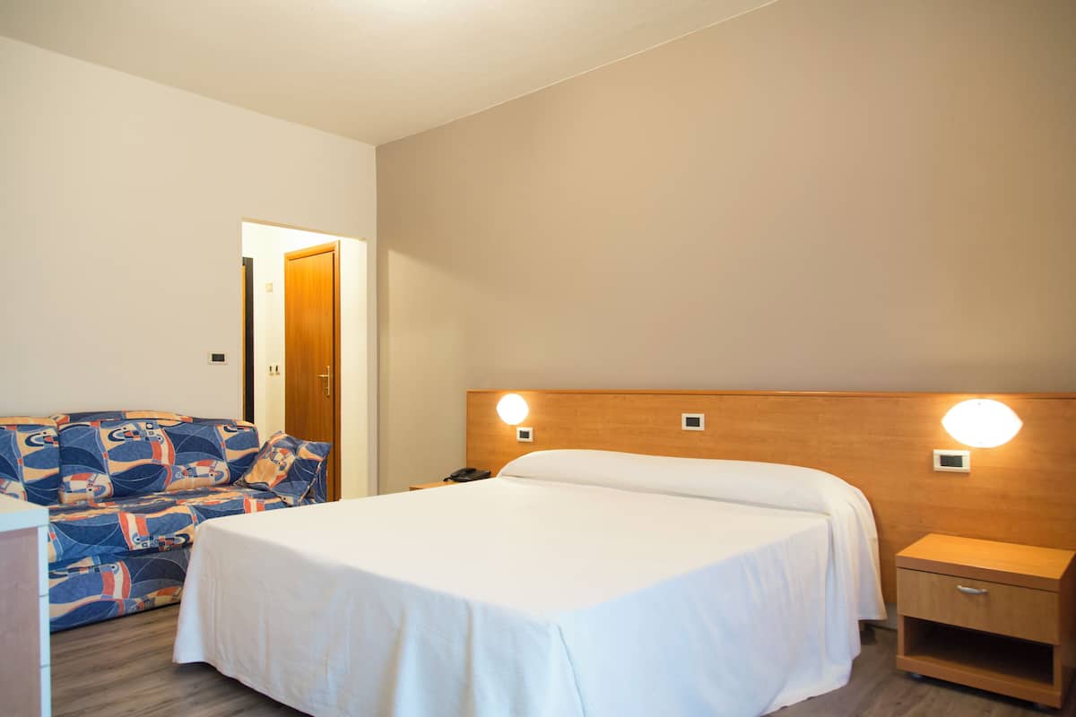 Une chambre d’hôtel avec un lit, un canapé, une table de chevet et une petite table.