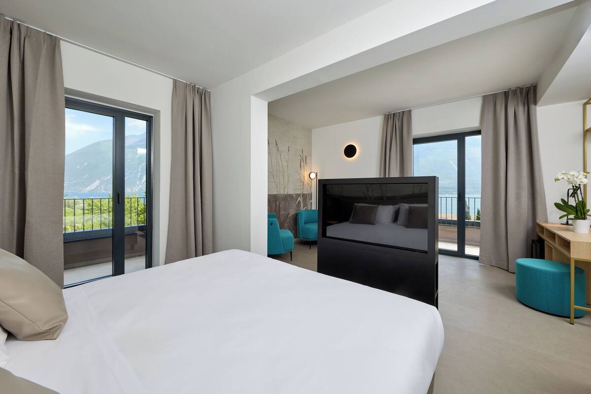 Une chambre d’hôtel moderne dotée d’un grand lit, d’un téléviseur à écran plat, d’un bureau avec une chaise et offrant une vue sur les montagnes par les fenêtres.