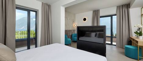 A modern hotel room with a large bed, a flat-screen TV, a desk with a chair, and a view of mountains through the windows.