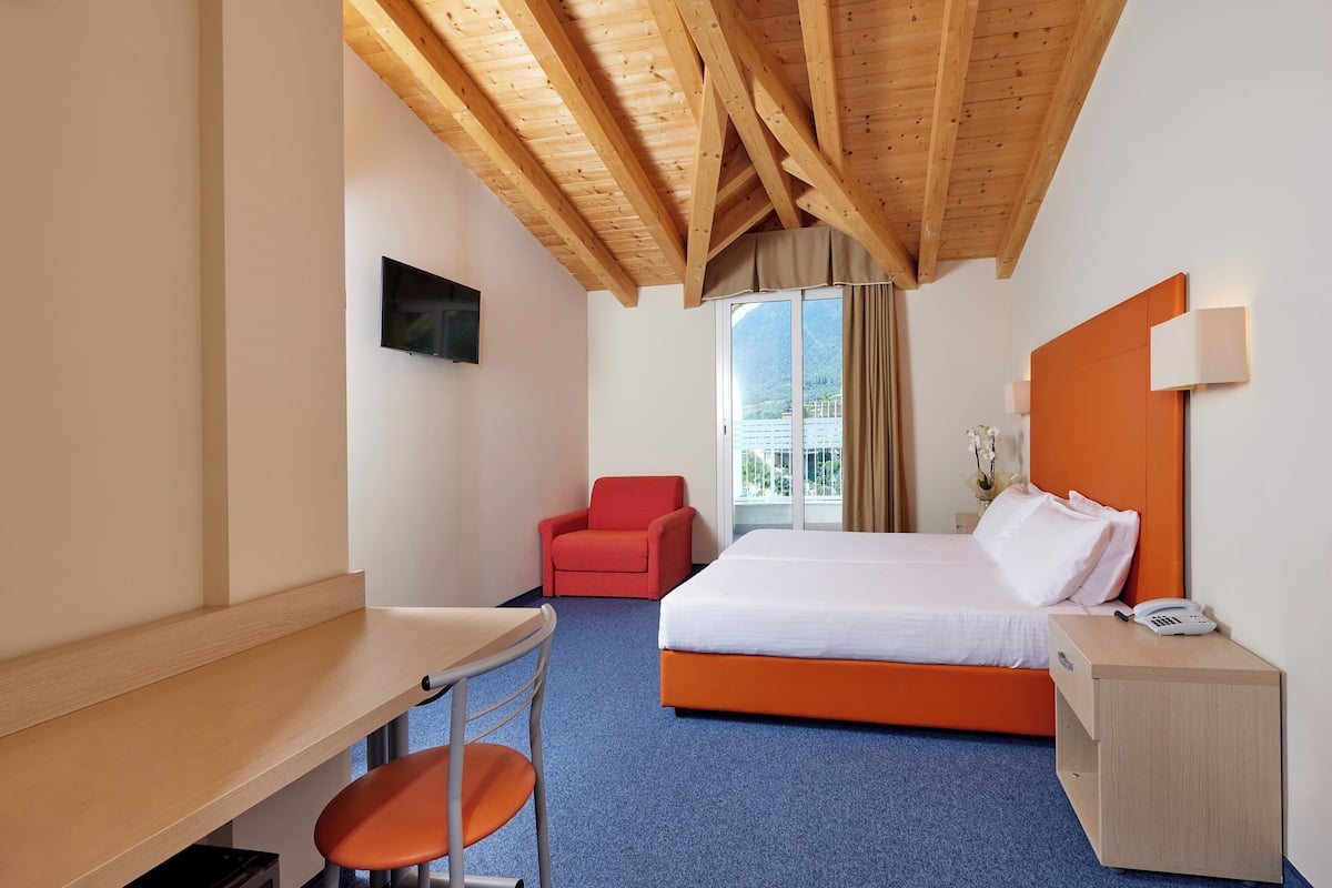 Une chambre d’hôtel avec un plafond en bois, un lit avec une tête de lit orange, un bureau avec une chaise et une fenêtre donnant sur les montagnes.