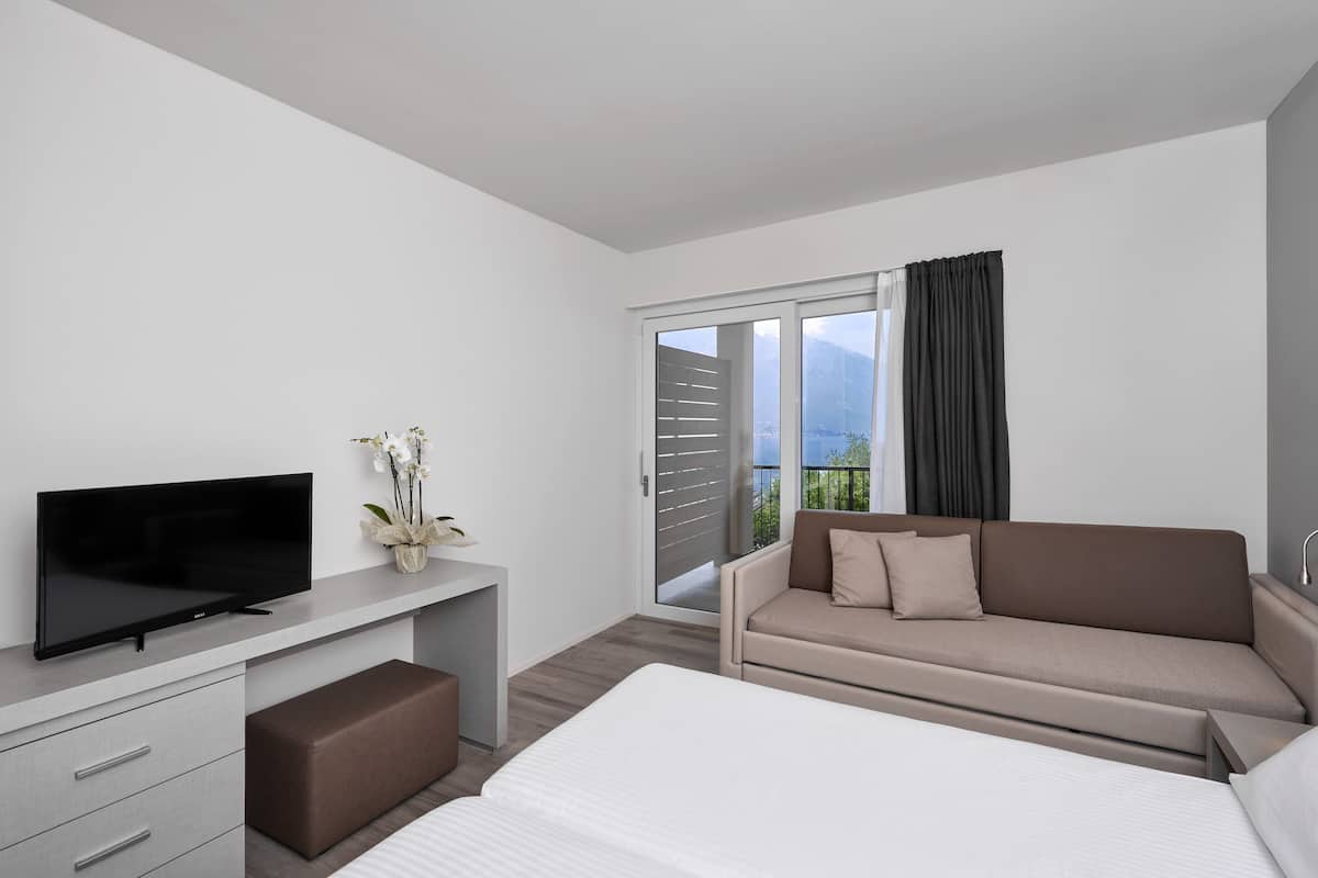 Une chambre d’hôtel moderne dotée d’une télévision à écran plat, d’un canapé, d’un lit et d’une porte-fenêtre coulissante donnant sur un balcon avec vue.