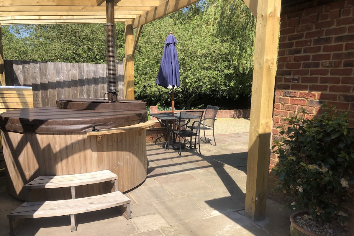 A covered patio area with a hot tub, wooden seating, and a table with chairs.