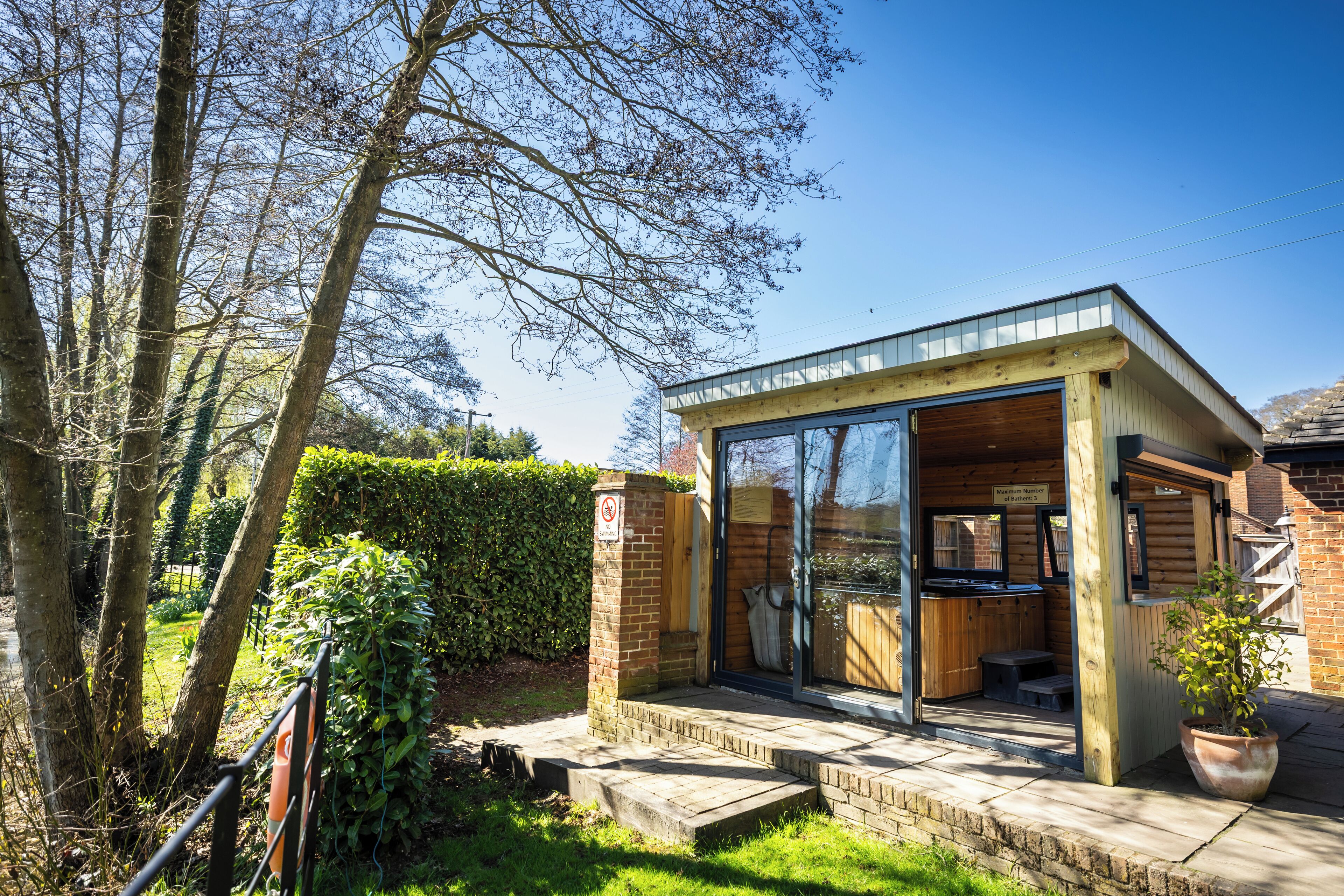 Een moderne buitenkeuken met glazen wanden, een houten terras en een bakstenen muur.