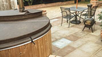 A hot tub with wooden steps, a table with chairs, and an umbrella.