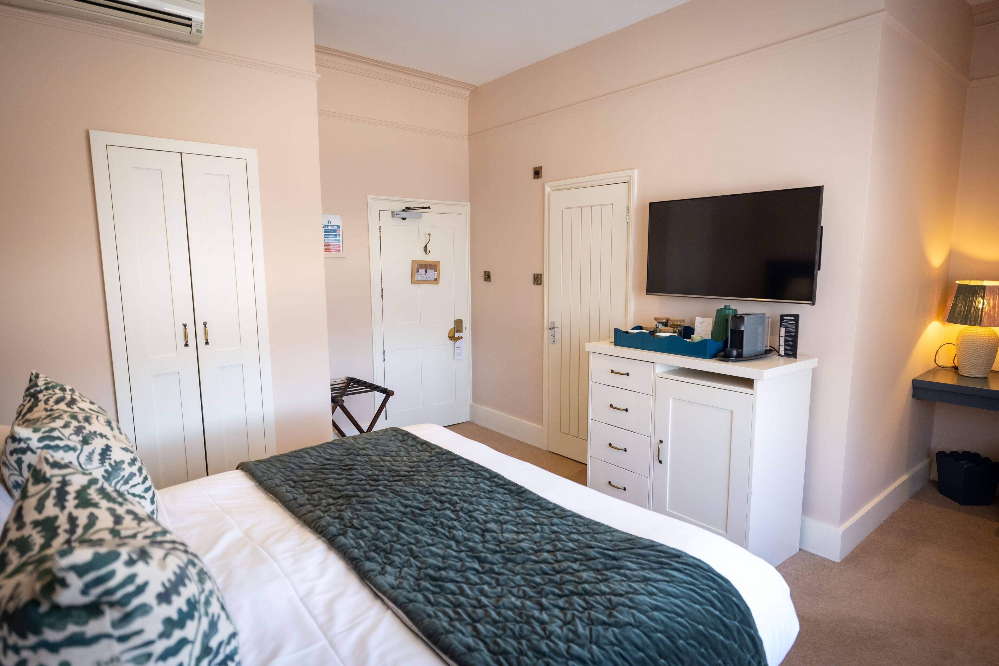 Ein Hotelzimmer mit Bett, Kleiderschrank, Fernseher und Schreibtisch mit Lampe.
