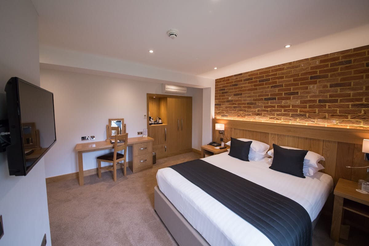 A hotel room with a large bed, a desk with a chair, a wardrobe, and a television.