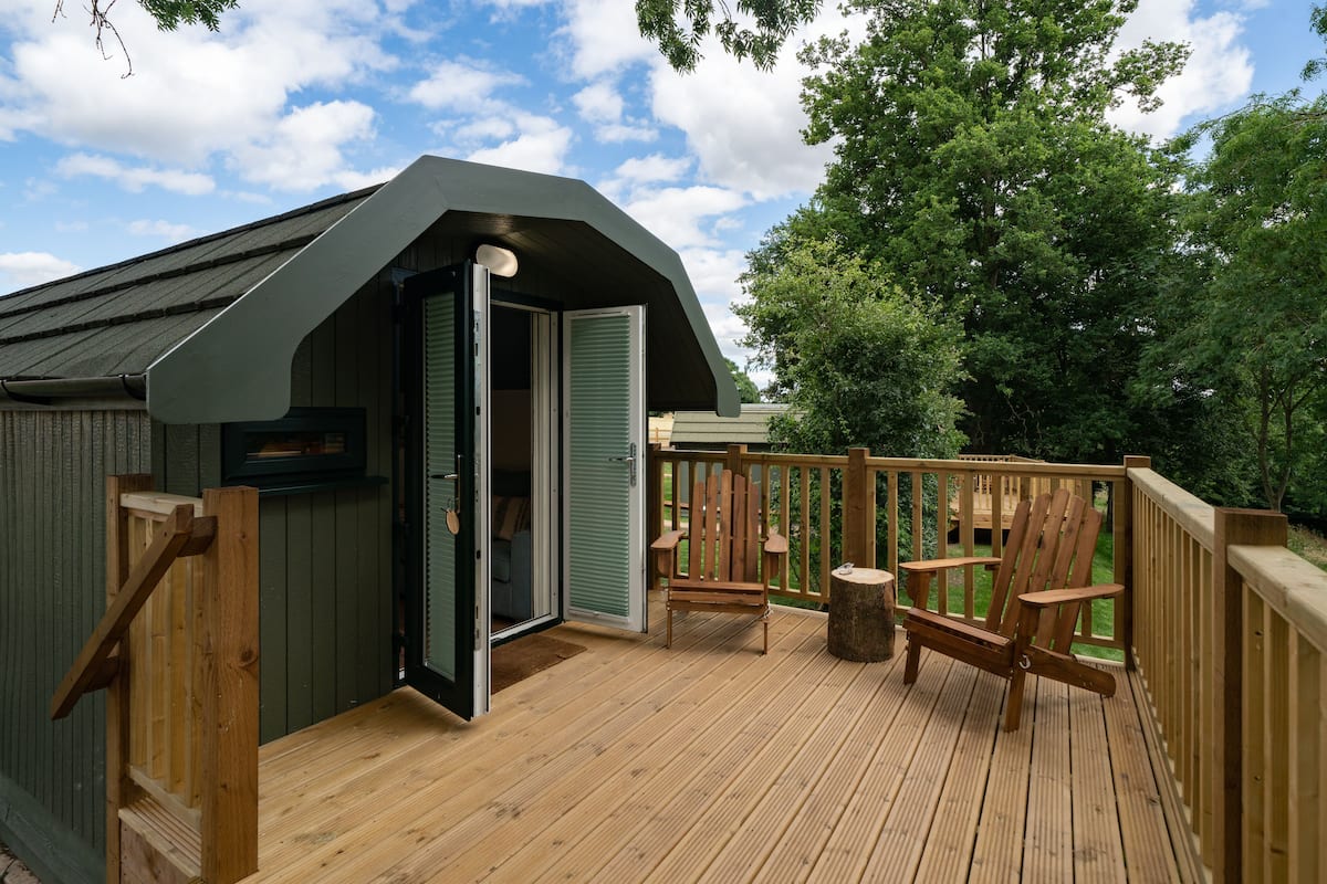 A wooden deck with two Adirondack chairs and a small wooden structure with a door.
