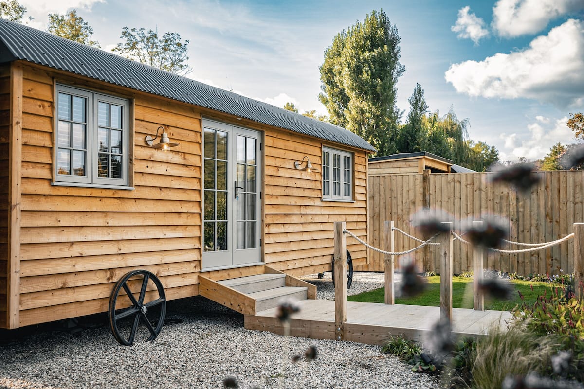 A wooden cabin with a metal roof, a front porch, and a gravel driveway.