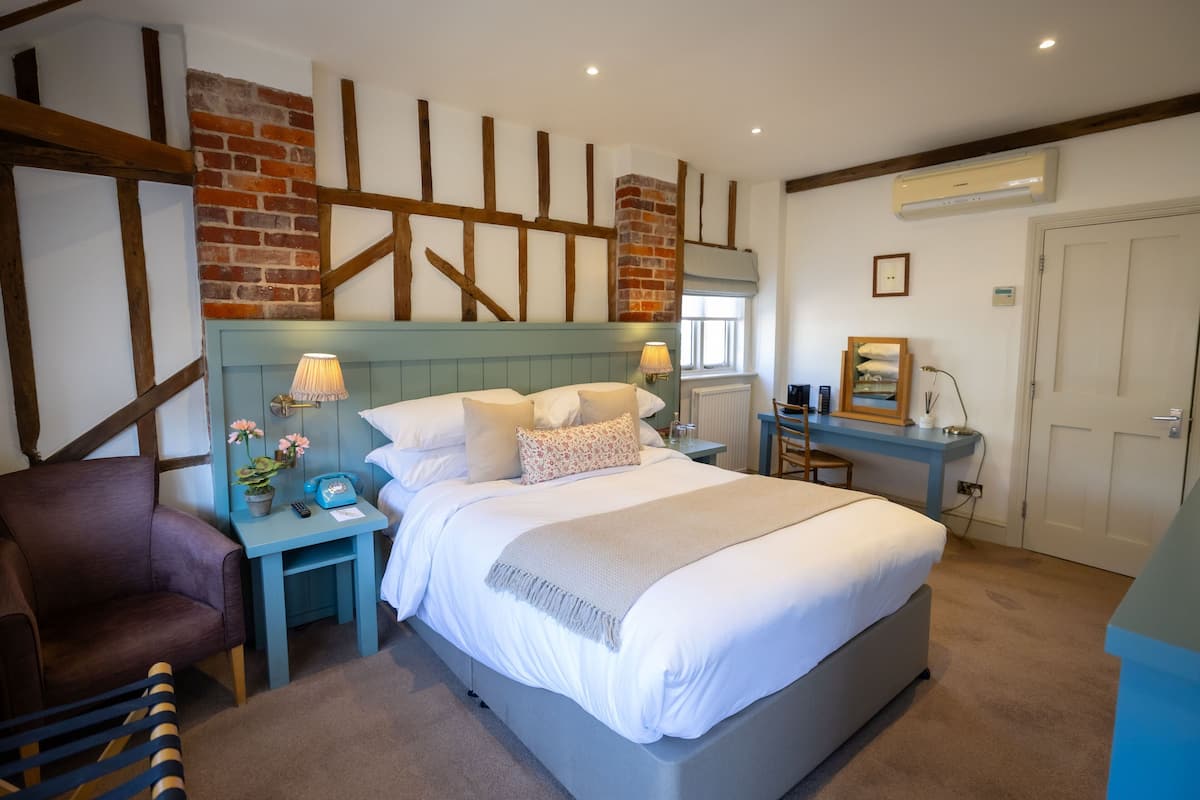 A bedroom with a large bed, a nightstand, a chair, a desk, and a brick wall.