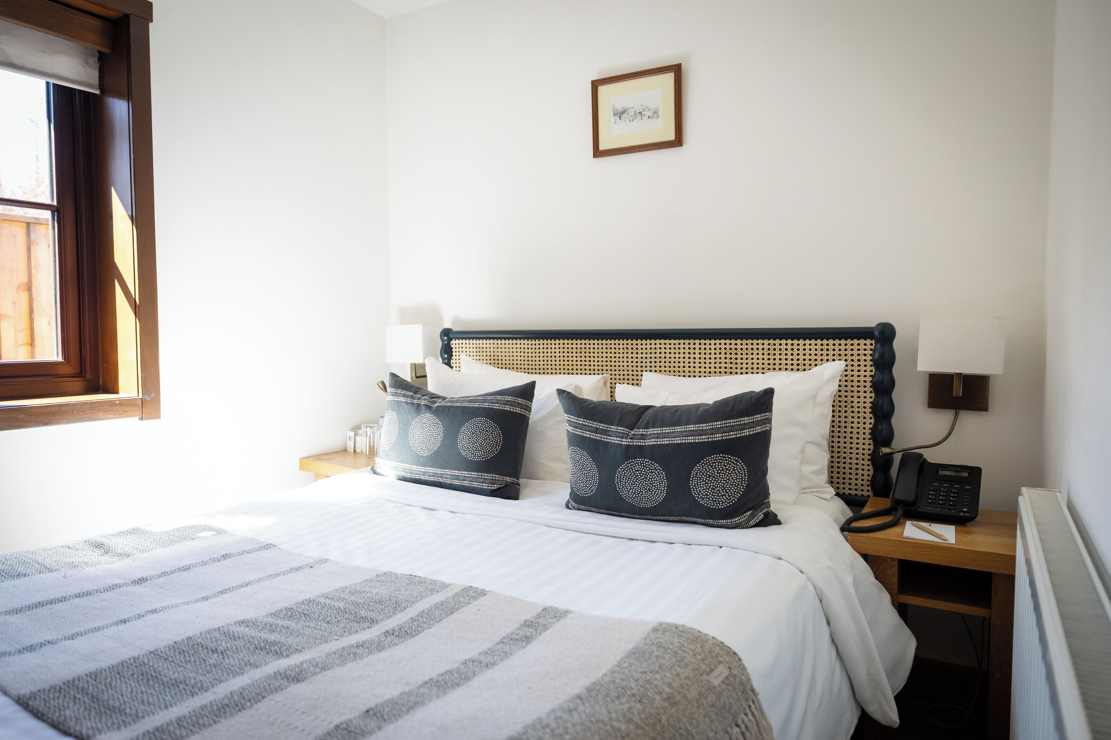 A neatly made bed with a striped blanket, a wooden headboard, and two bedside tables with lamps and a phone.