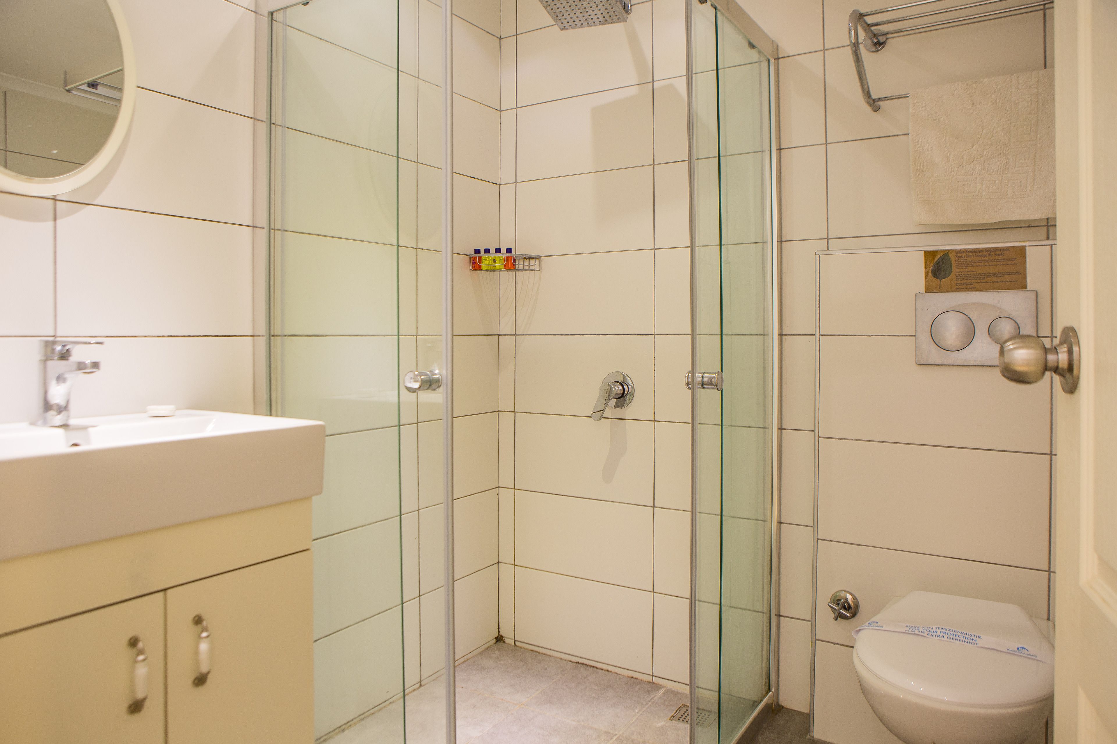 A bathroom with a glass shower enclosure, a toilet, and a sink with a mirror above it.