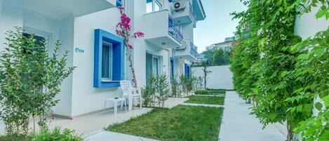 A white building with blue accents, a small garden area with a pathway, and a few potted plants.