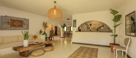 A spacious living room with a wooden coffee table, a sofa, a large potted plant, and a hanging light fixture.
