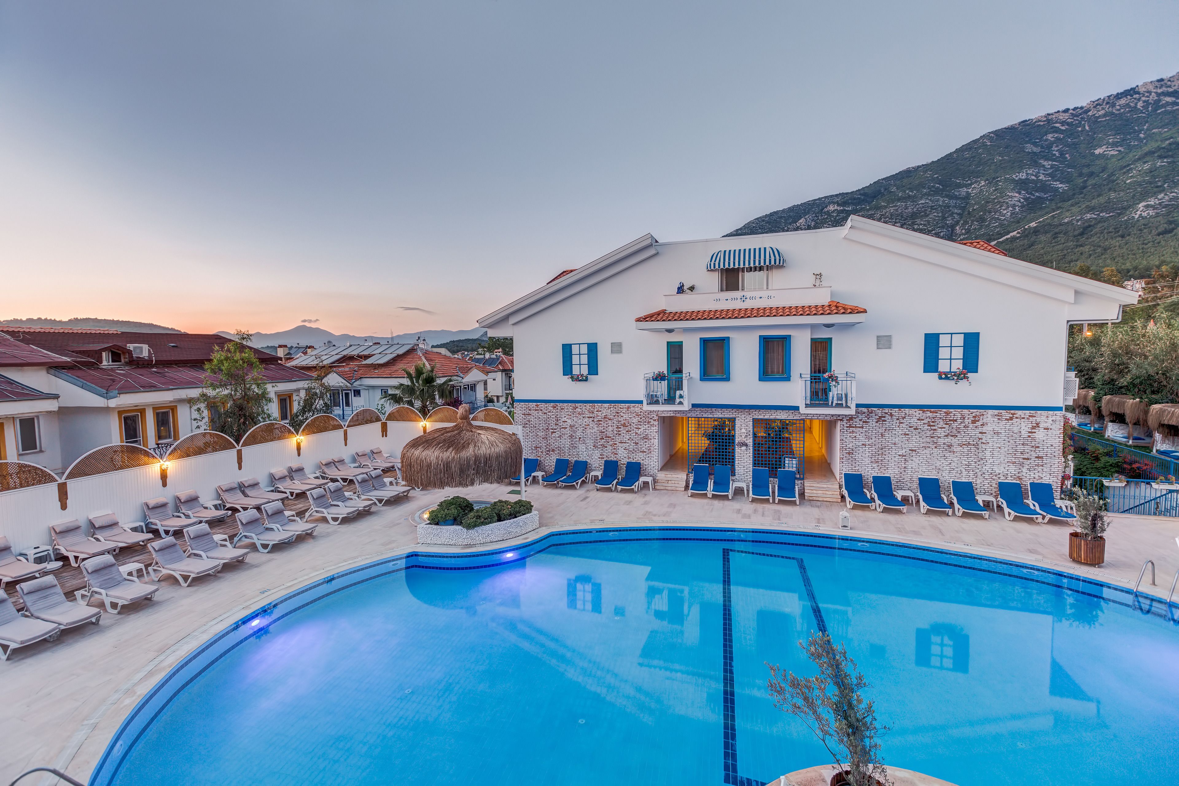 A resort with a swimming pool, sun loungers, and a mountain backdrop.