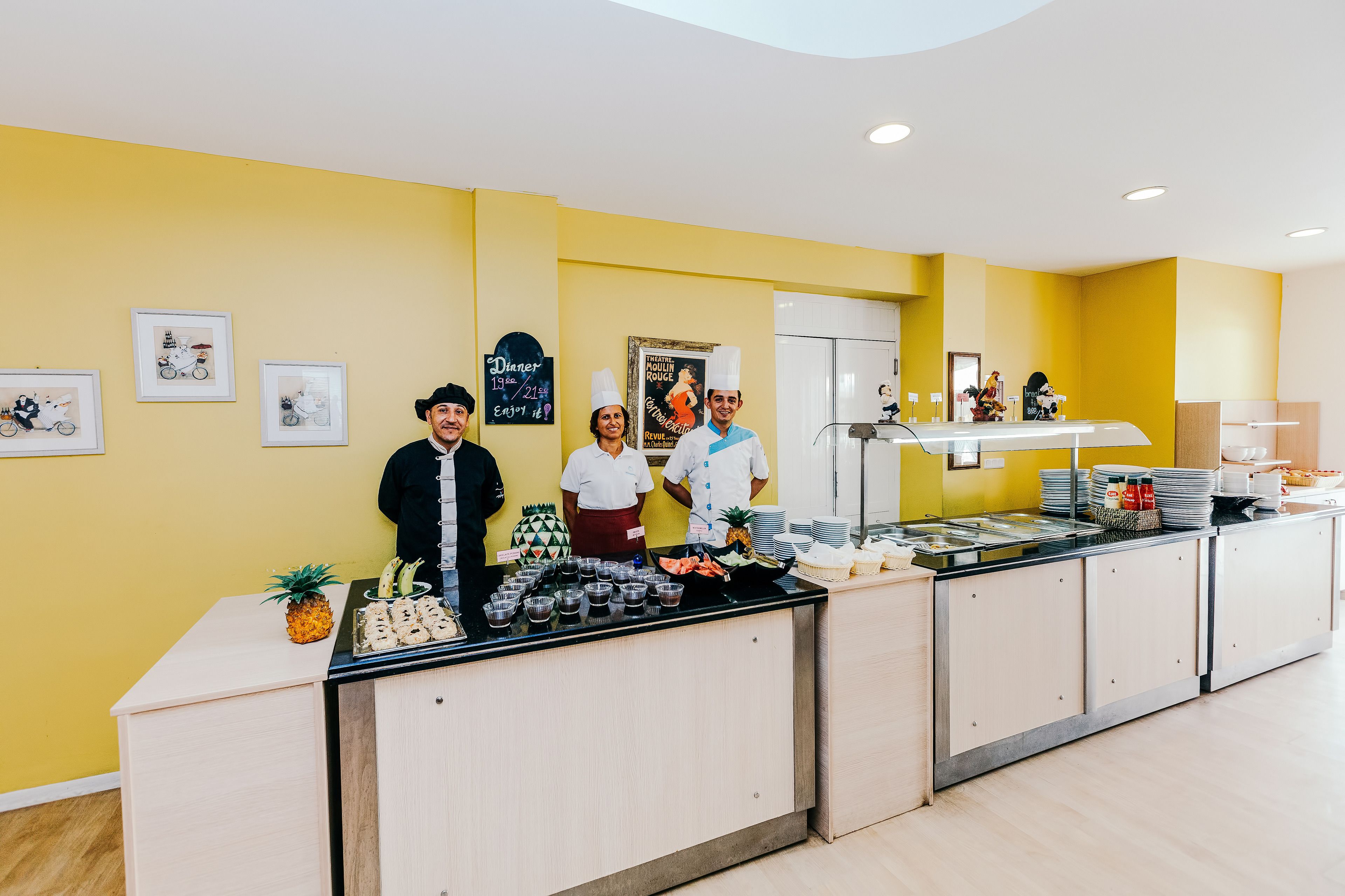 Angolo buffet con personale, pareti gialle e diversi tipi di cibo.