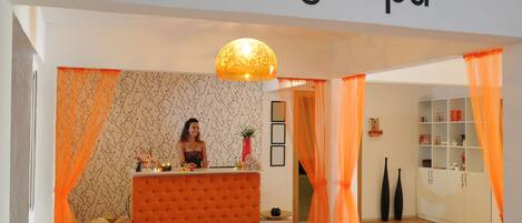 Interior de un spa con mostrador de recepción, un muro decorativo y estanterías.