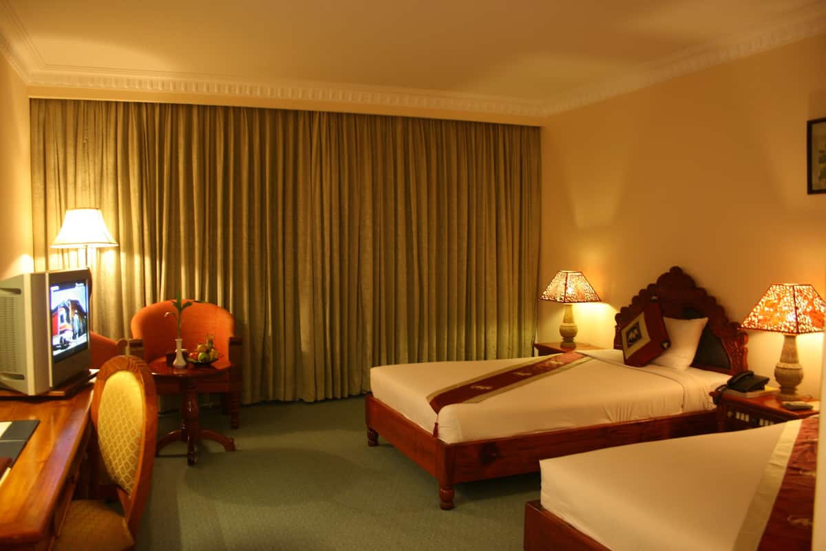 A hotel room with two beds, a desk with a television, and two lamps.