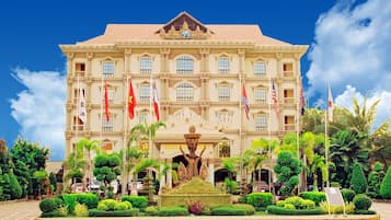 A large, ornate building with multiple flags, a central fountain, and well-maintained gardens.
