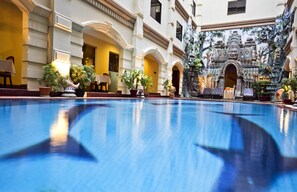 Una amplia piscina interior con reflejos, rodeada por un edificio de arquitectura clásica y fachada decorativa.