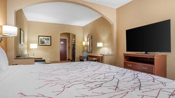 A hotel room with a large bed, a desk, a television, and a door leading to another room.