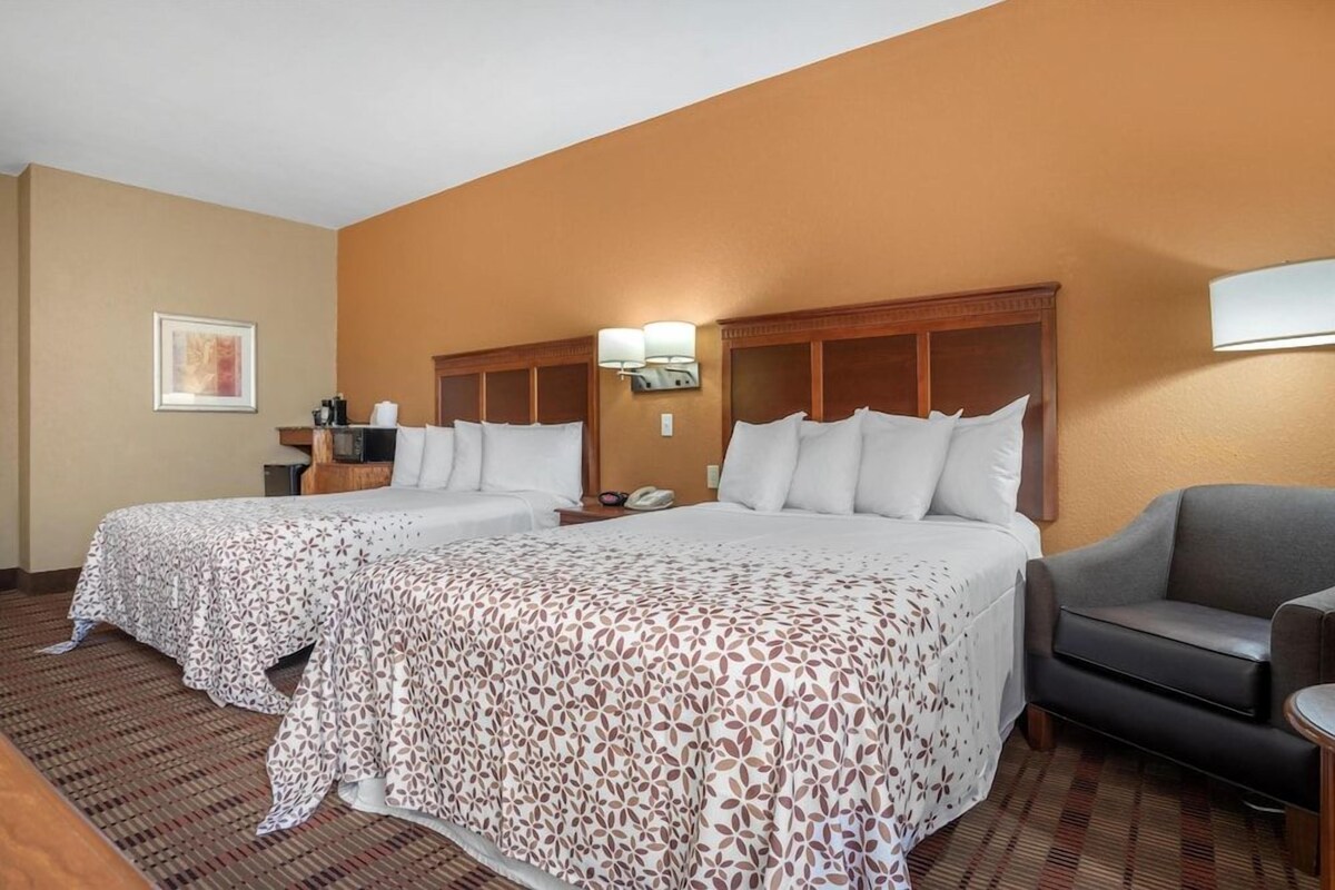 A hotel room with two beds, a sofa, a desk, and a lamp.