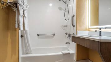 A bathroom with a white bathtub, a shower with a handheld showerhead, a towel rack with towels, a vanity with a mirror, and a toilet.