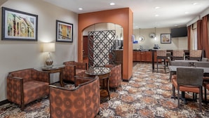 A hotel lobby with patterned armchairs, a coffee station, and artwork on the walls.