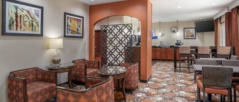 A hotel lobby with patterned armchairs, a coffee station, and artwork on the walls.