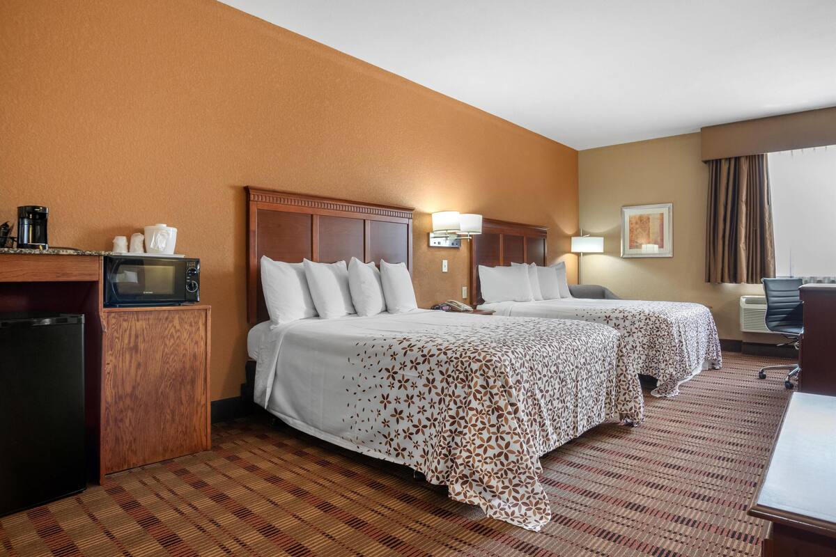 A hotel room with two beds, a desk, a microwave, and a refrigerator.
