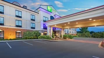Un Holiday Inn Express & Suites con cielo despejado, estacionamiento y entrada bien iluminada.