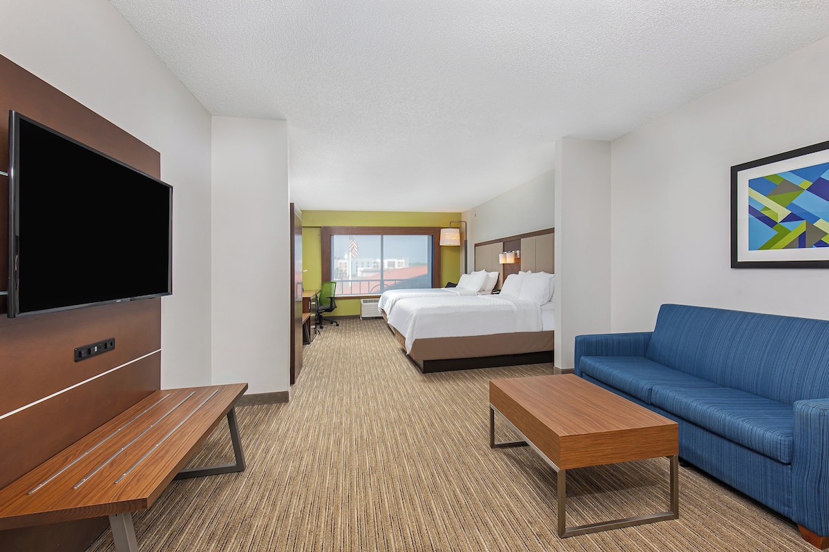 A hotel room with a bed, a blue sofa, a TV, a desk, and a carpeted floor.