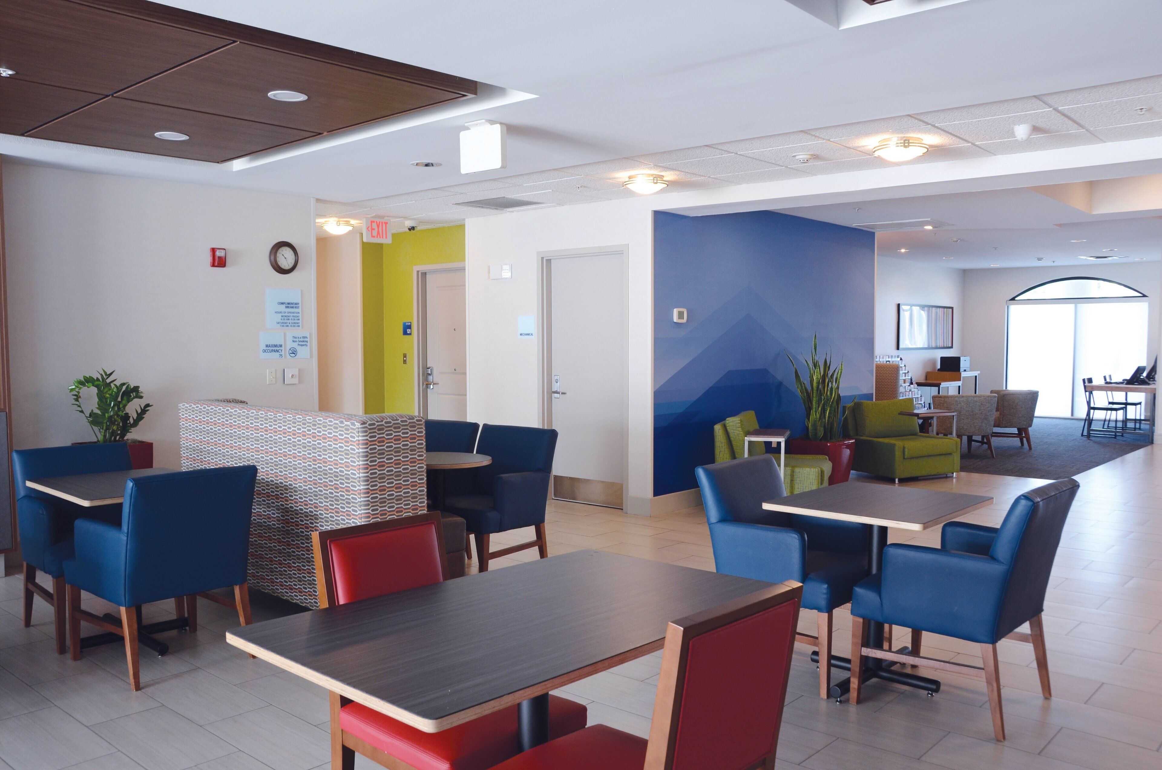 A modern indoor space with multiple seating areas, including tables and chairs, and a visible exit sign.