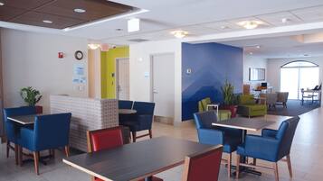 A modern indoor space with multiple seating areas, including tables and chairs, and a visible exit sign.
