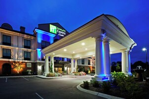A Holiday Inn Express & Suites hotel entrance with a covered walkway, clear signage, and a landscaped area with plants.